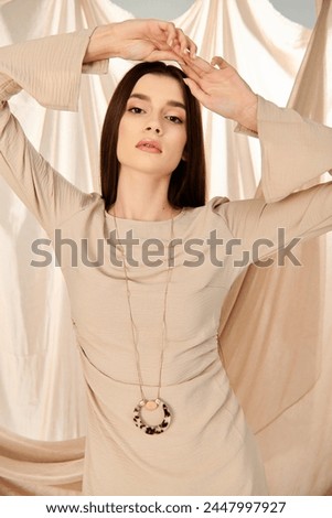 A young woman with long brunette hair poses gracefully in a beige dress, embodying a summer mood in a studio setting.