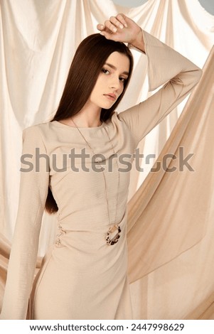 A young woman in a beige dress poses gracefully, exuding a summery vibe, against a studio backdrop.