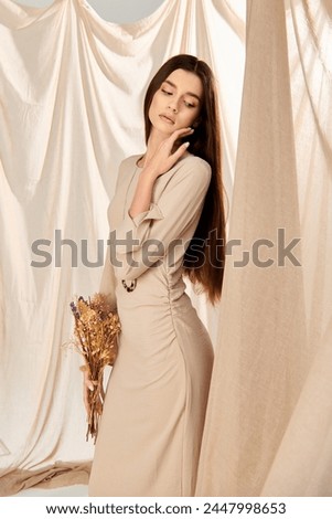 A young woman with long brunette hair strikes a pose in a summer outfit, exuding a sense of serenity in front of a white curtain.