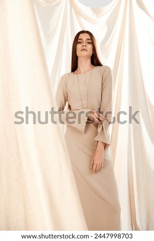 A young woman with long brunette hair stands gracefully in front of a billowy white curtain, embodying a sense of tranquil summer beauty. Royalty-Free Stock Photo #2447998703
