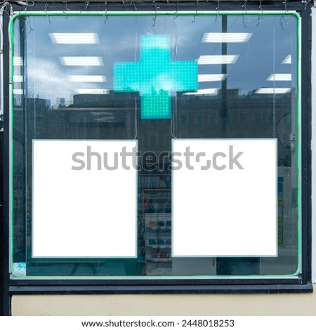 Pharmacy storefront with glowing green cross and two blank advertisement spaces. Reflection of urban environment on pharmacy window reveals city life outside.