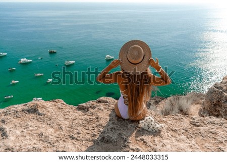 Woman travel sea. Happy woman in a beautiful location poses on a cliff high above the sea, with emerald waters and yachts in the background, while sharing her travel experiences Royalty-Free Stock Photo #2448033315
