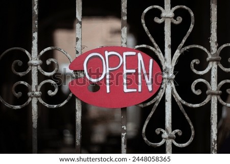 Handwritten Open sign on red oval wooden sign hangs on an old metal fence with peeling white paint. Artist's palette. Concept of permission to enter, opening, welcome, entry, hospitality, sale, trade
