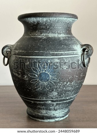 A metal jug made of bronze, gray-black with a bluish patina, with loops on the sides with round rings. Close-up photo. Stands on a wooden surface.