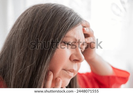 diseased mature woman experiences severe headache, holding head, Hot flashes during menopause, Decreased memory and concentration, feeling nervous, Feeling tired, exhausted, menopause, midlife crisis Royalty-Free Stock Photo #2448071555