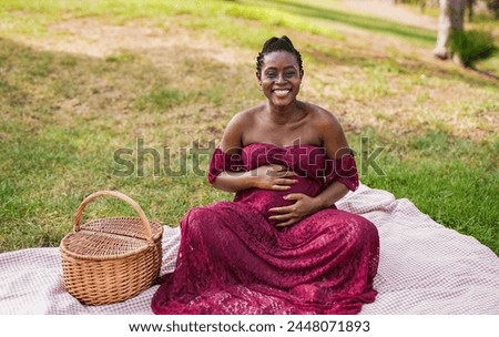 Happy pregnant african woman touching her belly while enjoy pic nic at park