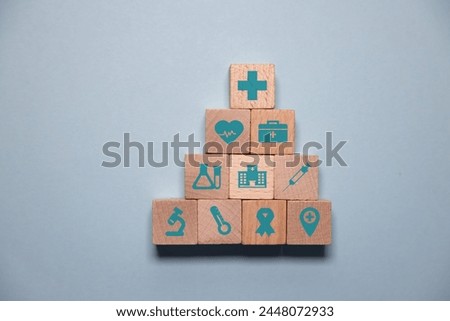 Pyramid wooden cubes, forming stack represents healthcare insurance concept. Medical icons atop, conveying protection and security. background provides copyspace for conveying Health Insurance ideas.
