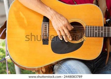 A man is playing a guitar with his hand on the fretboard. The guitar is a brown color and has a black fretboard Royalty-Free Stock Photo #2448083789