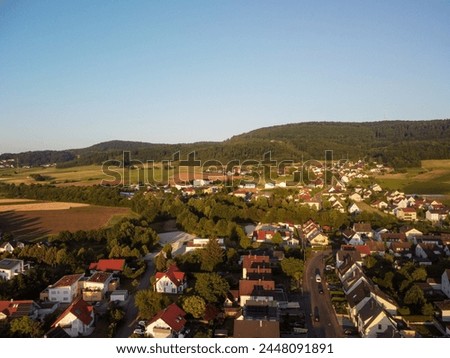 This stock photo shows a small town surrounded by fields and hills. The houses are mostly white with red roofs. The photo has a clear and sunny sky. german village photo drone shoot.
