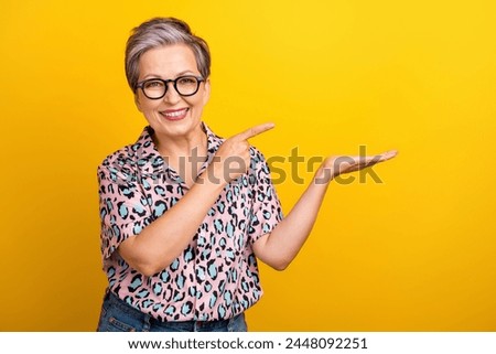 Photo of attractive pensioner woman hold point empty space dressed stylish leopard print clothes isolated on yellow color background