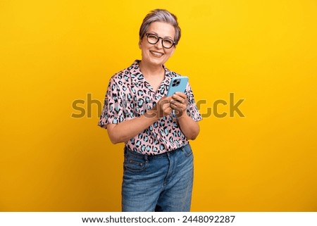 Photo portrait of pretty retired female hold telephone comment post wear trendy leopard print outfit isolated on yellow color background