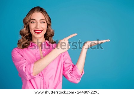 Photo portrait of pretty young girl hold point empty space wear trendy pink outfit hairdo isolated on blue color background