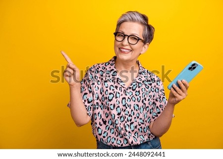 Photo portrait of lovely senior lady gadget point empty space dressed stylish leopard print garment isolated on yellow color background