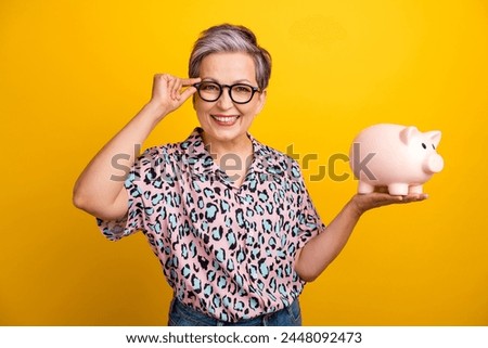 Photo portrait of pretty retired female hold piggy touch specs dressed stylish leopard print outfit isolated on yellow color background