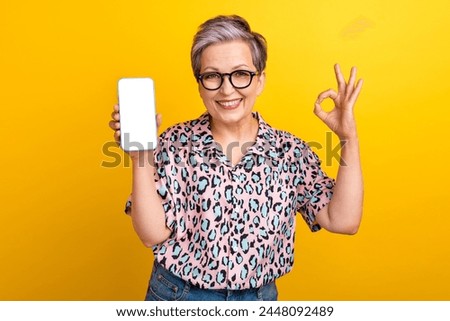 Photo portrait of lovely senior lady hold white screen show okey wear trendy leopard print garment isolated on yellow color background