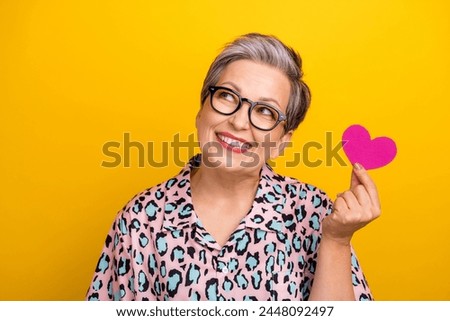 Photo portrait of pretty retired female look empty space hold heart wear trendy leopard print outfit isolated on yellow color background