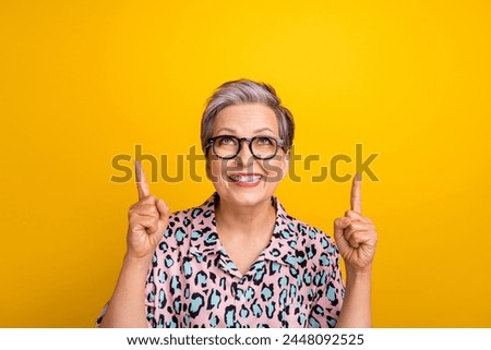 Photo portrait of pretty retired female look point up empty space wear trendy leopard print outfit isolated on yellow color background