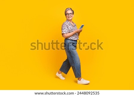 Full body photo of attractive pensioner woman hold device walking wear trendy leopard print clothes isolated on yellow color background