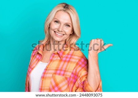 Portrait of toothy beaming woman blond hair dressed plaid shirt indicating at offer empty space isolated on turquoise color background