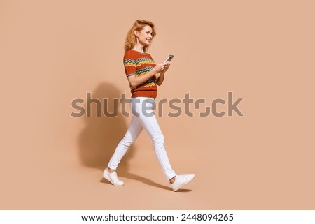 Full length photo of charming woman dressed knit t-shirt holding smartphone go look empty space isolated on pastel color background