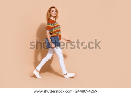 Photo portrait of lovely young lady hold netbook walking dressed stylish striped garment isolated on beige color background