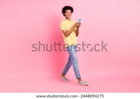 Full size photo of nice young man walk use smart phone wear yellow t-shirt isolated on pink color background
