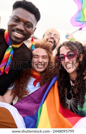 Vertical. A happy crowd of LGBT people wearing colorful smiling for a picture with a rainbow flag at a fun pride day parade event. They exude leisure and travel vibes. Community and friendship