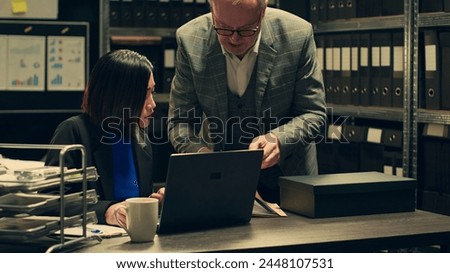 Forensic team examining clues and evidence stored in a case box, looking into surveillance photos to build suspects profile. Two detectives analyzes classified records in incident room. Camera A. Royalty-Free Stock Photo #2448107531