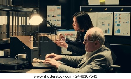 Inspector consulting with criminal expert on archived materials and autopsy records, examining folders and old cases to find connections. Private investigation in disability friendly space. Camera A. Royalty-Free Stock Photo #2448107543