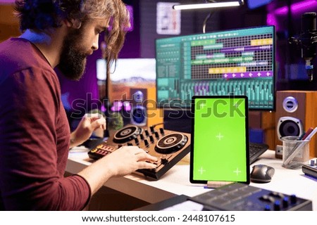 Composer creating soundtracks on stereo gear and greenscreen display on mobile device, mixing and mastering tunes in home studio. Young artist adjusting volume levels on music, daw software.