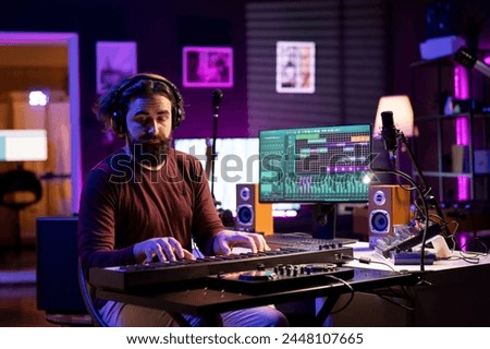Artist playing piano midi controller and recording new tunes, producing new electronic notes in his home studio. Sound engineer working on digital audio workstation interface, synthesizer keys.