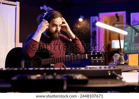 Sound composer operating with electronic setup in home studio, recording and playing acoustic guitar tunes. Musician working with signal processing techniques and audio plug ins at desk.