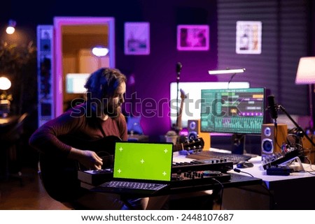 Musical performer playing acoustic guitar next to greenscreen layout on laptop, recording tunes using mixing console and daw software. Artist trying new accords on instrument, music industry.