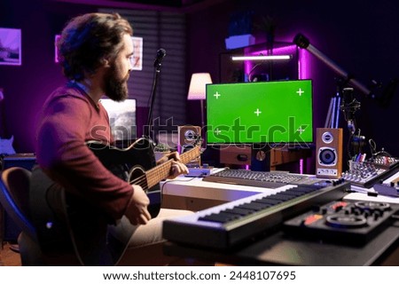 Artist learning to play guitar with internet lessons on greenscreen monitor, watching tutorials for acoustics rehearsal in home studio. Producer learns new string accords for music industry.