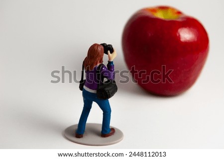 photographer action figure toy taking a photo of a giant apple
