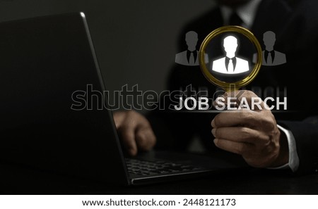 A man is holding a magnifying glass over a laptop screen that says Job Search. Concept of searching for a job, and the mood is serious and focused