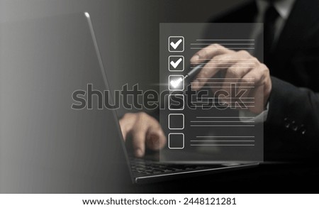 A man is typing on a laptop with a check mark on a list. The man is wearing a suit and tie