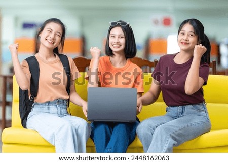 Group of 3 Asian female students, excited and happy that they passed the final exam and got excellent grades, have laptops in the university library, sitting on sofas, wearing casual clothes with bags Royalty-Free Stock Photo #2448162063