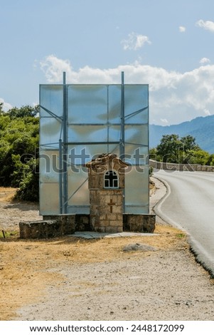 A roadside shrine in front of backside of road sign beside a winding road, in Meteora, Greece.
