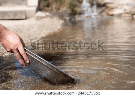 Searching for gold with an iron pan in a riverbed. Gold panning Royalty-Free Stock Photo #2448175563
