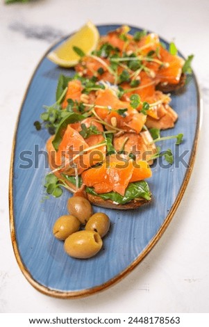 salmon with lemon, olives and microgreens on a blue plate on the table.