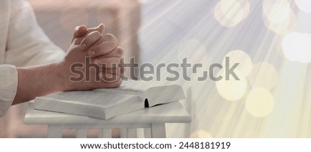 Religion. Christian man praying over Bible at table, closeup. Bokeh effect. Banner design