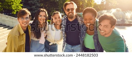 Panoramic portrait photo of multinational company of happy friends on walk on sunny summer day in city park. Attractive young people look into camera and smile. Concept of youth lifestyle, friendship.