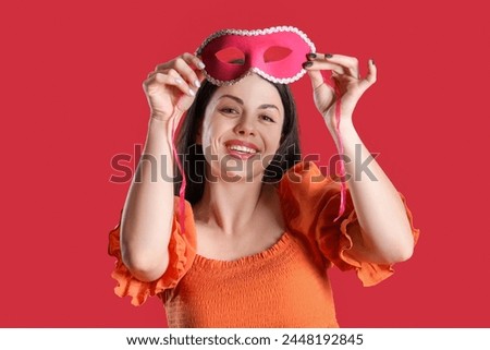 Happy young woman with carnival mask on red background