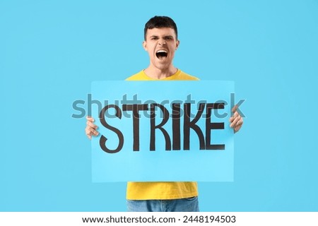 Protesting young man holding placard with word STRIKE on blue background