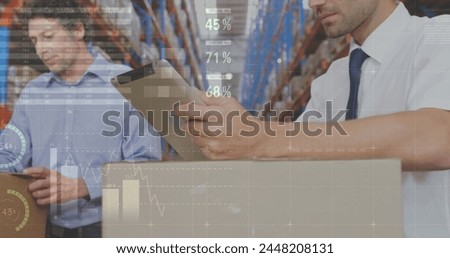 Close up of two Caucasian workers  writing on clip board in a distribution warehouse. Digital image of graphs and statistics are seen in the foreground
