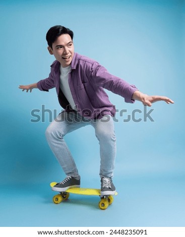 Photo of younf Asian man skating on blue background