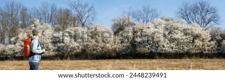 Bird watching. Woman ornithologist with binoculars observes birds arriving in spring in blooming nature. Panoramic view Royalty-Free Stock Photo #2448239491