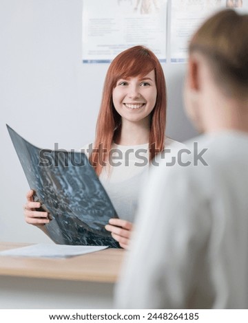 Woman doctor orthopedic with MRI picture in hands smiles at patient. physiotherapist explains diagnosis using x-ray at table. traumatologist tells good news to patient. Front view. White background.