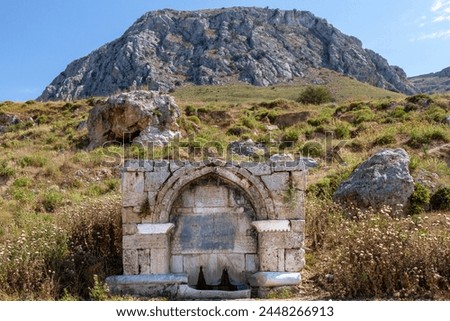 Medieval stone fountain at the base of Acrocorinth hill, in Ancient Corinth, Greece. It was built in 1515 and has ottoman inscription on it.  Royalty-Free Stock Photo #2448266913